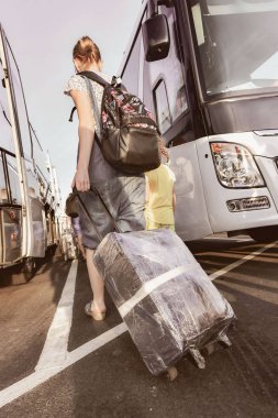 Çocuk kızla otobüs ile seyahat. O onunla bir sırt çantası ve tekerlekli bavula vardır.