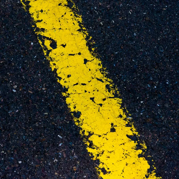 Yellow diagonal strip of paint on black new asphalt.