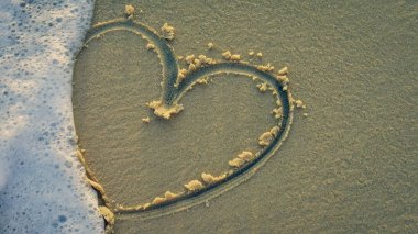 Sahilde bir kalp ve arka planda dalgalar.