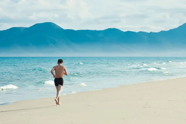 男人早上锻炼。沿着海岸线的沙滩跑步。复制文本的空间。越南 图库照片