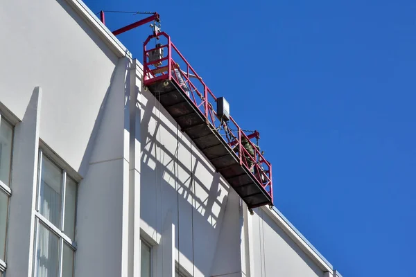 Berceau spécialement équipé sur la façade du bâtiment. Déplace verticalement le long de la façade pour effectuer des réparations et nettoyer le bâtiment . Images De Stock Libres De Droits