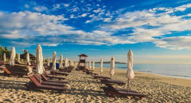 Boş bir kumsalda şezlonglar ve şemsiyeler. Yaz güneşli bulutlu mavi gökyüzü. Cam Ranh. Vietnam.