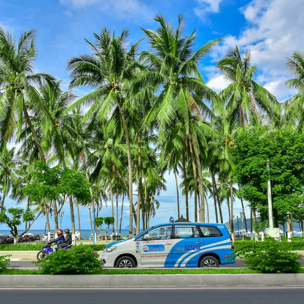 12 juillet 2018. Vietnam. Nha Trang. Taxi voiture bleu et blanc promenades sur la route de la côte de la mer. Le long de la route palmiers et autres plantes tropicales — Photo