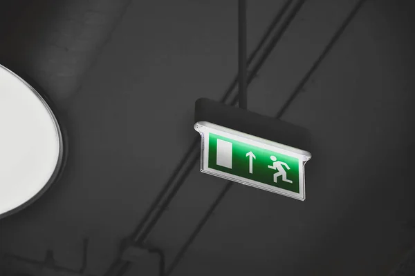 illuminated green exit sign suspended from the ceiling in a public facility