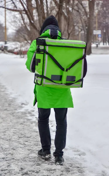 De bezorger loopt door de straat. Hij draagt een groene overall en een speciale rechthoekige transport rugzak. Mock up blank voor tekst en reclame — Stockfoto