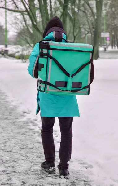 Teslimatçı sokakta yürüyor. O mavi tulum ve özel bir dikdörtgen taşıma sırt çantası giyiyor. Metin ve reklam için boş alay — Stok fotoğraf