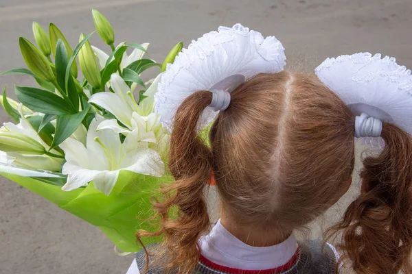 Une fille avec de grands arcs blancs sur la tête, une belle coiffure. Elle a un bouquet de lis. Elle allait aller à l'école le 1er septembre. Vue de l'arrière gros plan Images De Stock Libres De Droits