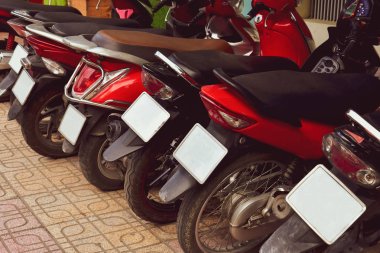 Sokakta park edilmiş birçok kırmızı moped ve scooter motosikleti. Bisiklet numaraları taklit için silindi