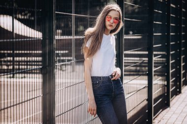 Sokakta duran pikn gözlüklü beyaz t-shirt, kot, giyen güzel ve genç birbayan. Moda fotoğraf yakınında demir çit