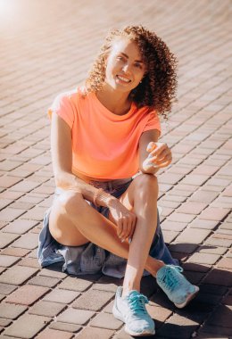 Kıvırcık kadın gülüyor ve yere oturur. Gülümseyen kadın ile bukleler eğleniyor. t-shirt aralığı. Yaşam tarzı ve saç modeli kavramları