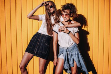 Görüntü iki şık mutlu kadın arkadaş. gözlük ve sarı duvardan ayakta kot giyen.