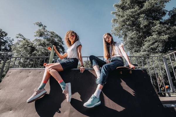 Kaykay ile paten parkta oturan iki kadın arkadaş.