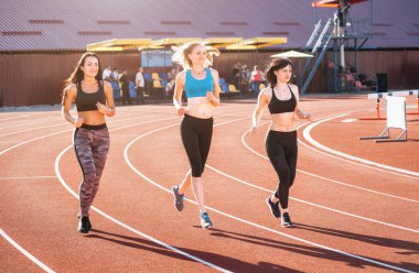 Atletizm yarış pistinde Futbol Stadyumu üzerinde çalışan ve rekabet ve sporda liderlik kavramı temsil eden sporcu kadın grubu