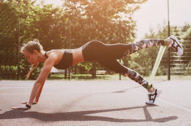 Genç sportif kadın lastik bantla dışarıda egzersiz yapıyor.