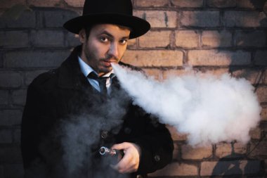 Genç hipster adam sigara veya elektronik sigara vaping. Bir kravat ve siyah şapka giyen adam. Lezzetli çiftleri. Buhar bulutu.