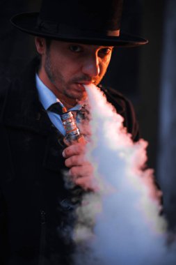 Genç hipster adam sigara veya elektronik sigara vaping. Bir kravat ve siyah şapka giyen adam. Lezzetli çiftleri. Buhar bulutu.