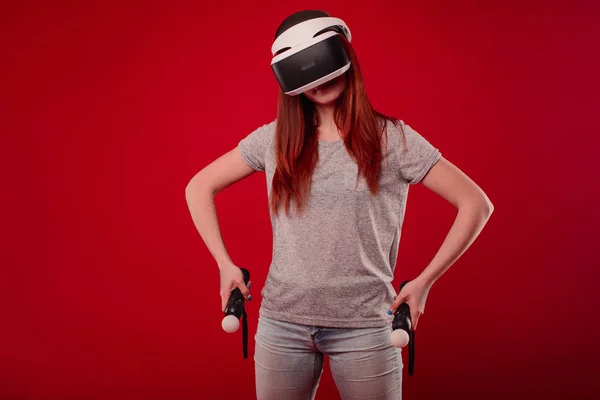Hermosa mujer con gafas de realidad virtual en el estudio. Persona con casco de realidad virtual aislado sobre fondo rojo. Mujer joven sorprendida tocando el aire durante la experiencia VR — Foto de Stock