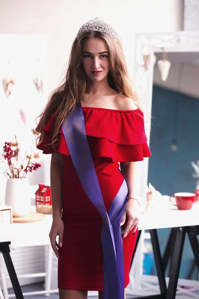 Модна студія фото красивої усміхненої жінки з довгим волоссям носить розкішне червоне плаття і дорогоцінну корону. переможець конкурсу краси — стокове фото