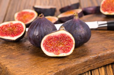 Grup tüm ve dilimlenmiş Olgun, lezzetli ve tatlılar incir eski bir rustik ahşap kesme tahtası üzerinde bir mutfak bıçağı ile