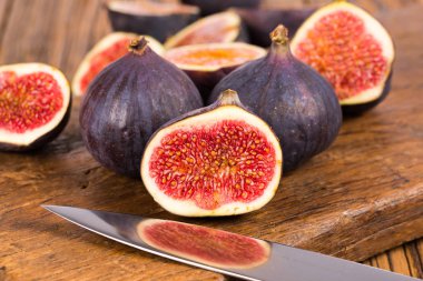 Grup tüm ve dilimlenmiş Olgun, lezzetli ve tatlılar incir eski bir rustik ahşap kesme tahtası üzerinde bir mutfak bıçağı ile