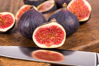 Grup tüm ve dilimlenmiş Olgun, lezzetli ve tatlılar incir eski bir rustik ahşap kesme tahtası üzerinde bir mutfak bıçağı ile