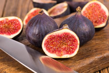 Grup tüm ve dilimlenmiş Olgun, lezzetli ve tatlılar incir eski bir rustik ahşap kesme tahtası üzerinde bir mutfak bıçağı ile