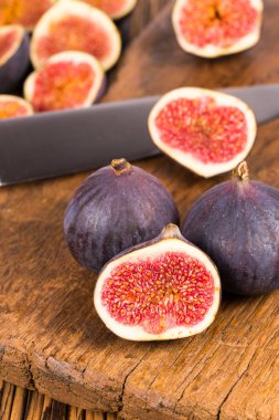 Grup tüm ve dilimlenmiş Olgun, lezzetli ve tatlılar incir eski bir rustik ahşap kesme tahtası üzerinde bir mutfak bıçağı ile