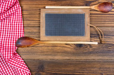 İki eski ahşap kaşık ve eski bir tahta tahtası ve kırmızı ve beyaz ekoseli bir kumaş kırsal bir ahşap arka planda kendi dizaynınız için metin alanı ile yatar..