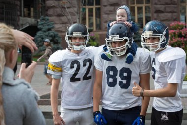 Players in American football are photographed with the child during the physical culture and sports day on Khreschatyk street in Kiev, Ukraine. September 12, 2015. clipart