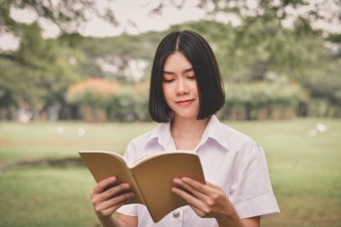 Eğitim kavramları. Güzel öğrenci parkta kitap okuma. Güzel kız parkta rahatlatıcı. Genç öğrenci okumak mutlu. Çalışmaya genç öğrenci aşk. Asyalı kadınların eğitim.