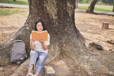 Eğitim kavramları. Asyalı kadın parkta kitap okuma. Güzel kadın parkta rahatlatıcı. Güzel kadınlar okumak mutlu olur.