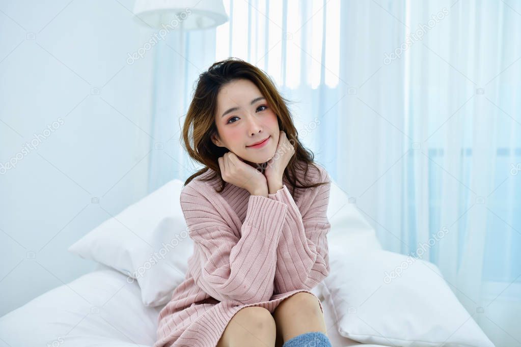 Winter Concept. Beautiful woman is relaxing in  bedroom.  Woman wearing a sweater in white bedroom.