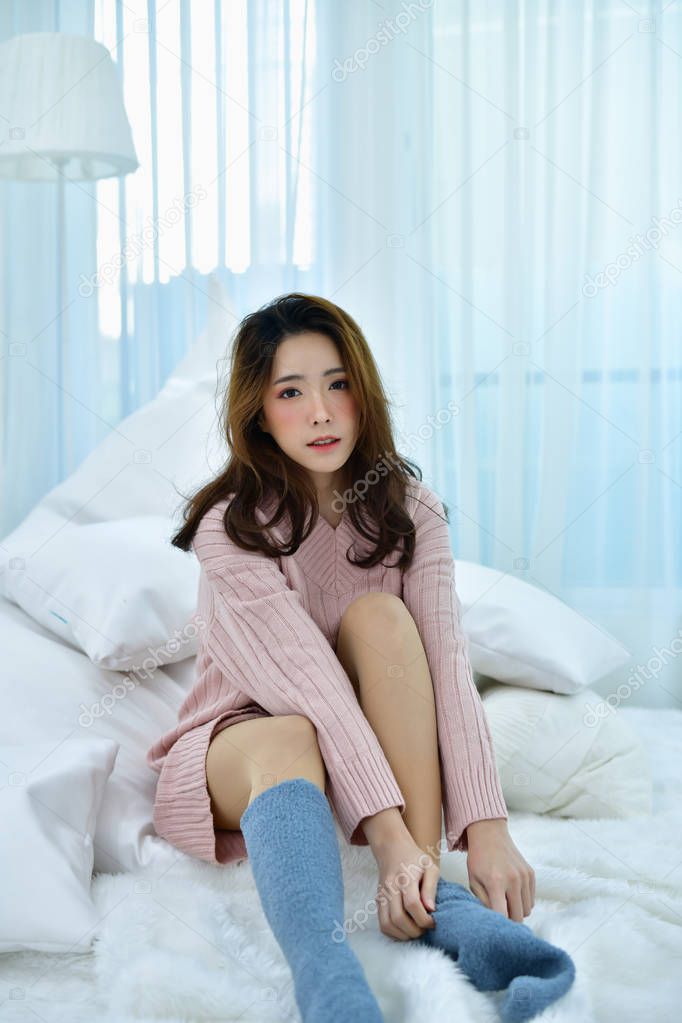 Winter Concept. Beautiful woman is relaxing in  bedroom.  Woman wearing a sweater in white bedroom.