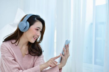 Kış konsepti. Şirin Asyalı kız kış elbise. Kış giysileri güzel kadın yatak odasında müzik dinlemek.