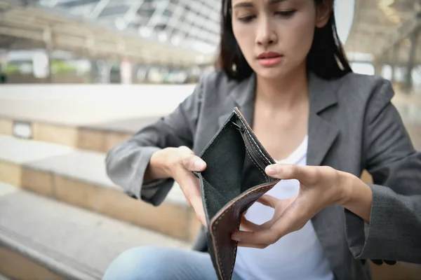 Concept of unemployed. Asian businesswoman is opening empty wallet. Young business woman is stressed because of no money.