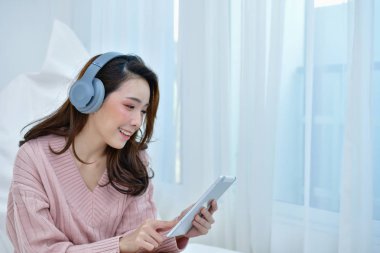 Kış konsepti. Şirin Asyalı kız kış elbise. Kış giysileri güzel kadın yatak odasında müzik dinlemek.