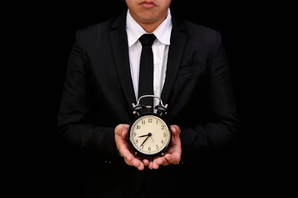 Business concept. Businessman holding a clock on a black background.