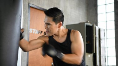 Egzersiz konsepti. Genç adam spor salonunda kum torbalarını yumruklıyordu.