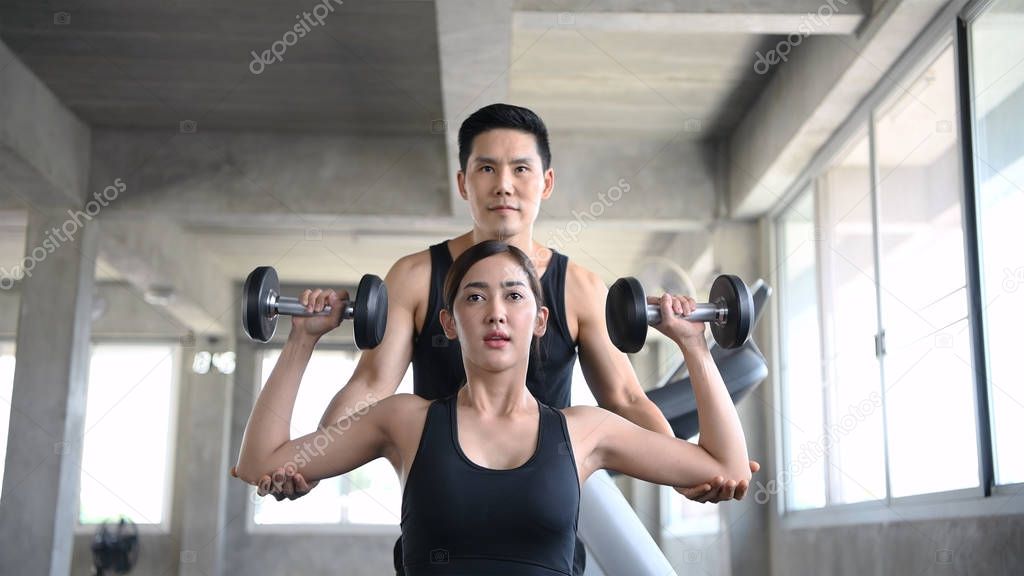 Sports concept. The girl is training dumbbells with the trainer 