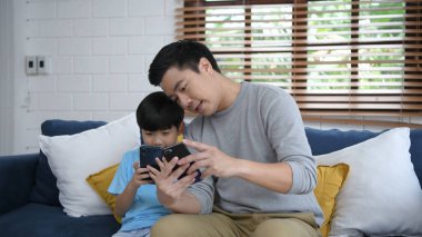 Aile kavramı. Baba ve oğul evde cep telefonu oynuyorlar. 4k Çözünürlüğü.
