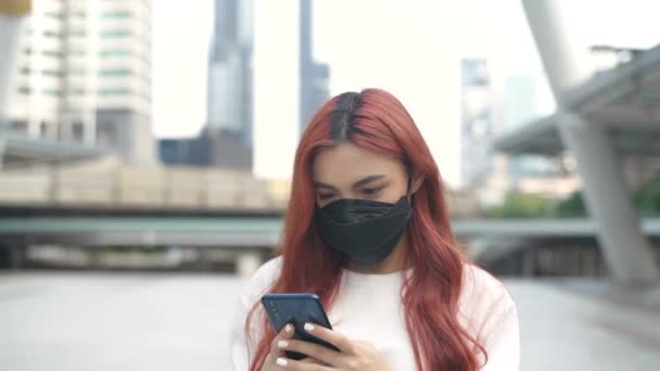 マスクをした赤い髪に染まった女性が 街中の携帯電話で遊んでいる 4K分解能 — ストック動画