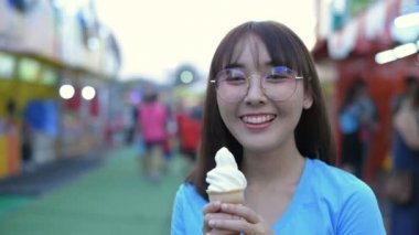 Tatil konsepti. Kız lunaparkta dondurma yemekten zevk alıyor. 4k Çözünürlüğü.