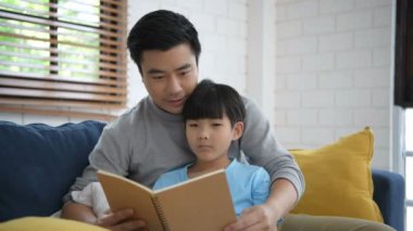 Aile kavramı. Baba oğluna evde bir kitap okumayı öğretiyor. 4k Çözünürlüğü.