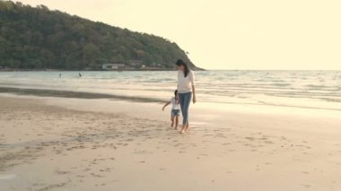 Aile kavramı. Anne deniz kenarında yürümesi için kızını tutuyor. 4k Çözünürlüğü.