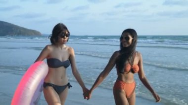 Tatil konsepti. Bikinili iki güzel kız sahilde geziniyor. 4k Çözünürlüğü.
