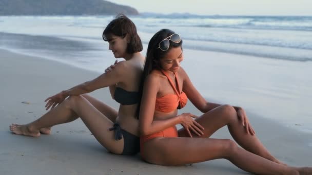 假期的概念 两个穿着比基尼的漂亮姑娘正在海滩上涂奶油 4K分辨率 — 图库视频影像