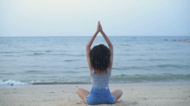 Tatil konsepti. Güzel kız sahilde yoga yapıyor. 4k Çözünürlüğü.