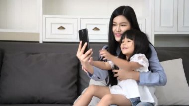 Aile kavramı. Anne ve kızı oturma odasında fotoğraf çekiyorlar. 4k Çözünürlüğü.