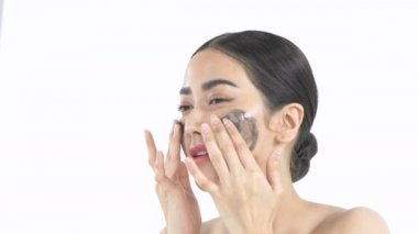 Yüzüne yüz kremi süren genç bir kadın. Taze cildi mükemmel olan güzellik mankeni beyaz arka plandaki cildine önem verir. 4k Çözünürlüğü.