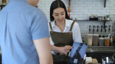 Kahve dükkanı konsepti. Kasiyer ürünü tezgahtaki tablet aracılığıyla öneriyor. 4k Çözünürlüğü.